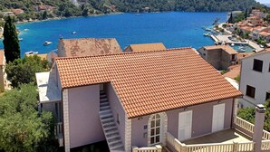 Un edificio costero con techo de tejas rojas, una escalera y vistas a una bahía con barcos.