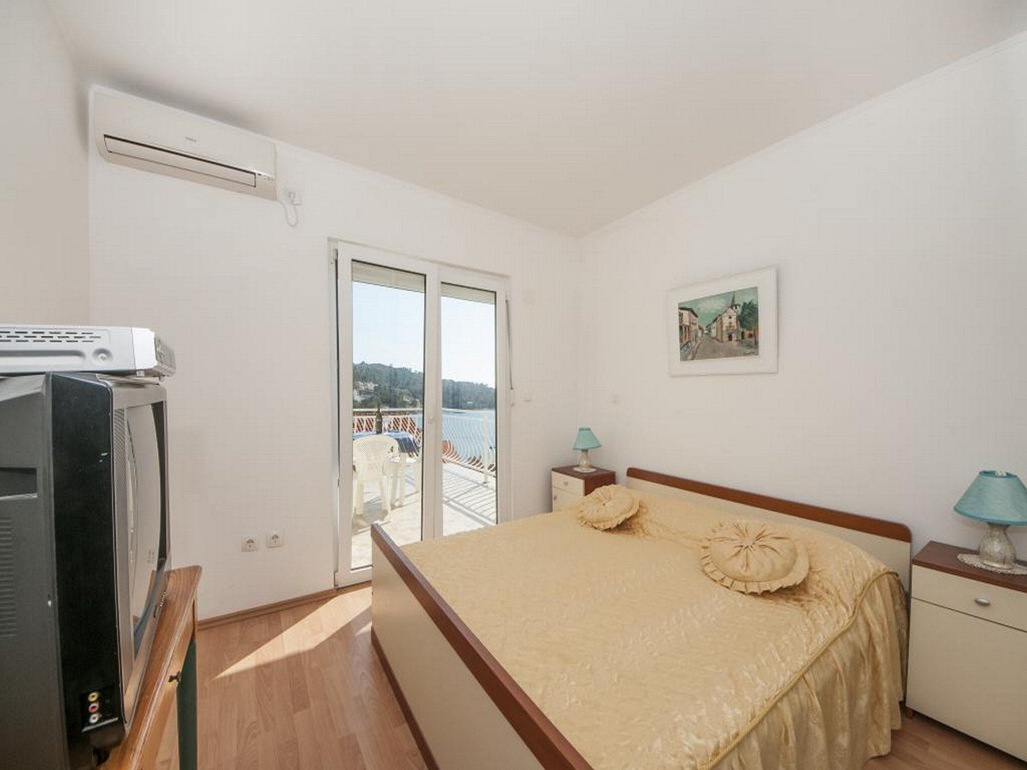 Un dormitorio con cama, televisión, balcón con vistas y un cuadro en la pared.