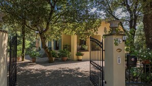 A gated entrance to a building with a gravel driveway, surrounded by trees and potted plants. - Villa Rinaldi 6 in Carpineta (Monteriggioni)