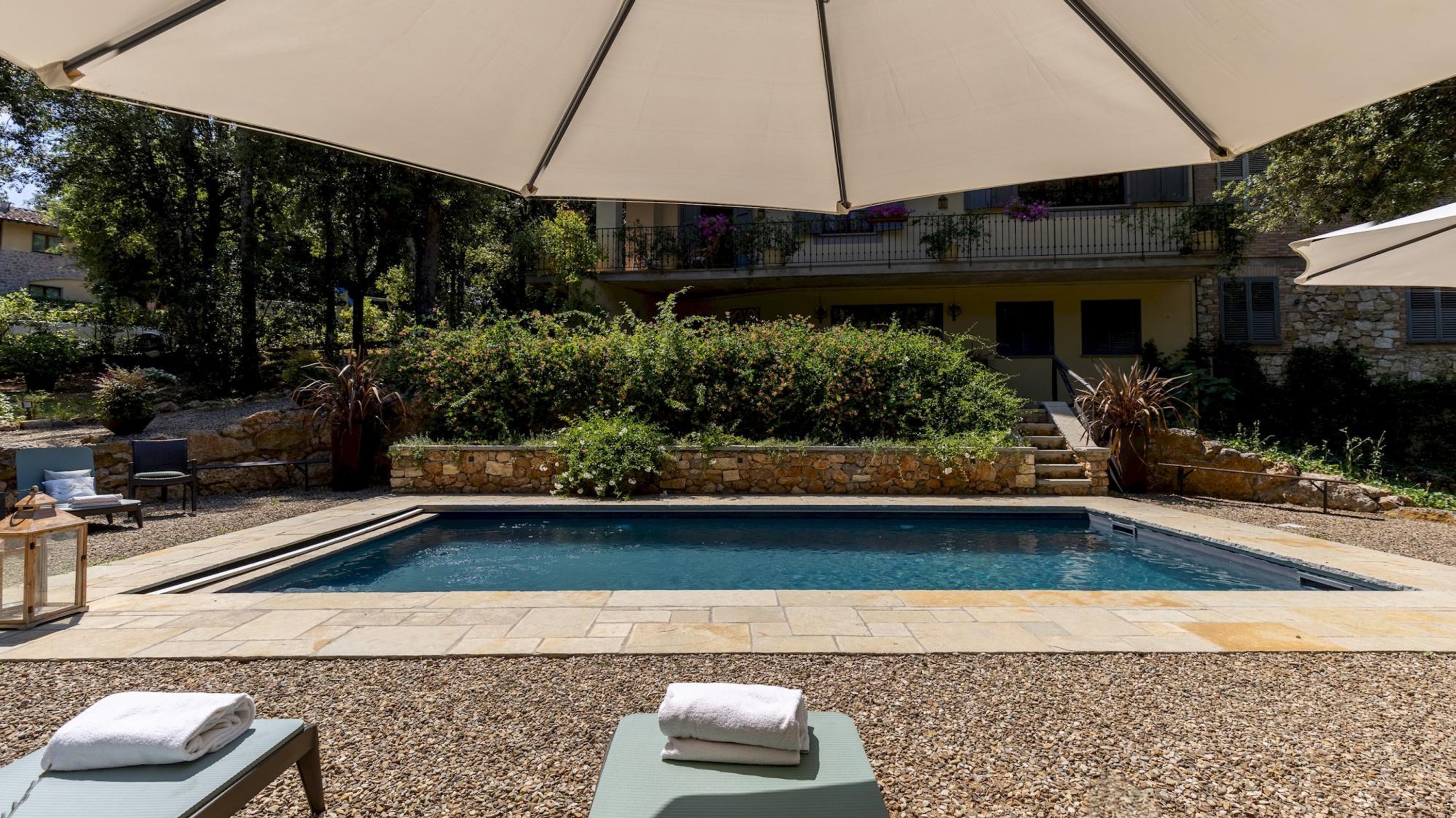 Una piscina con solárium de piedra, rodeada de vegetación y una pérgola que ofrece sombra.