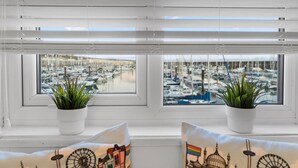 A window with two potted plants and two pillows with cityscape prints. - On the Water 4 By My Getaways (Brighton)