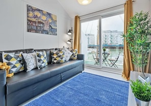 A modern living room with a sofa adorned with patterned cushions, a blue rug, and a cityscape painting on the wall. - On the Water 4 By My Getaways (Brighton)