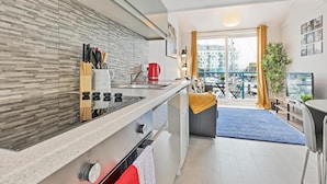 A modern kitchen with a built-in stove, a coffee machine, and a dining area with a blue rug and yellow curtains. - On the Water 4 By My Getaways (Brighton)