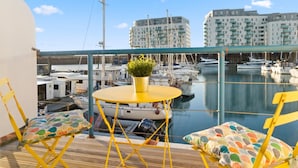 A balcony with yellow chairs and a small table, overlooking a marina with boats and buildings in the background. - On the Water 4 By My Getaways (Brighton)