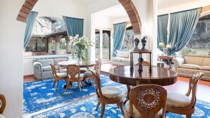 A spacious living room with a round wooden table, blue patterned sofas, and a large blue patterned rug. - Villa Mimmina 8 in Civitella in Val di Chiana (Civitella in Val di Chiana)