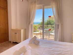 A hotel room with a bed, a wooden wardrobe, and a view of the sea through a glass door. - Villa Madrid Private Pool by Casasol (Nerja)