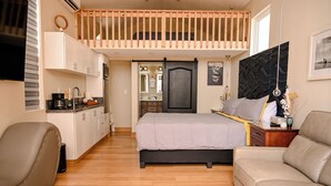 Ein Schlafzimmer mit Bett, Sofa, Schlafgalerie aus Holz, Küchenzeile und Bad.