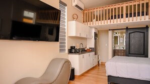 Ein gemütlicher Raum mit Bett, Stuhl, Küchenzeile und Fernseher.
