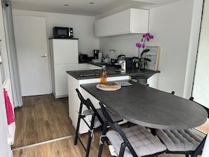 Eine kleine Küche mit Mikrowelle, Toaster und Kaffeemaschine. Im Vordergrund steht ein Tisch mit Stühlen.