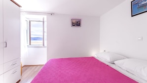 A bedroom with a bed, a window, a wardrobe, and a framed picture on the wall. - First row to the sea (Baska)