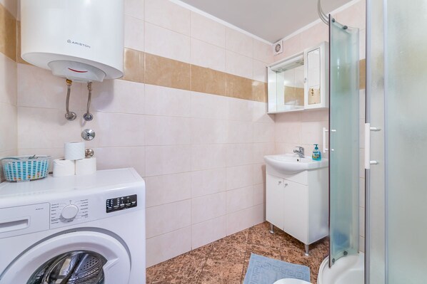 Ein kleines Badezimmer mit Waschmaschine, Waschbecken und einer Duschkabine aus Glas.