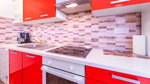 A modern kitchen with red cabinets, a black stove, and a tiled backsplash. - First row to the sea (Baska)