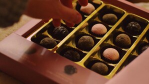 A hand selecting a truffle from a box. - Iconic Residency (New Delhi)