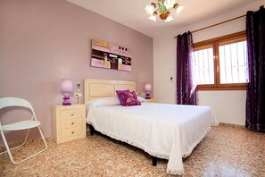 A bedroom with a bed, nightstands, a chair, a wall art piece, and a window with curtains. - Spacious Home in Teulada (Teulada)