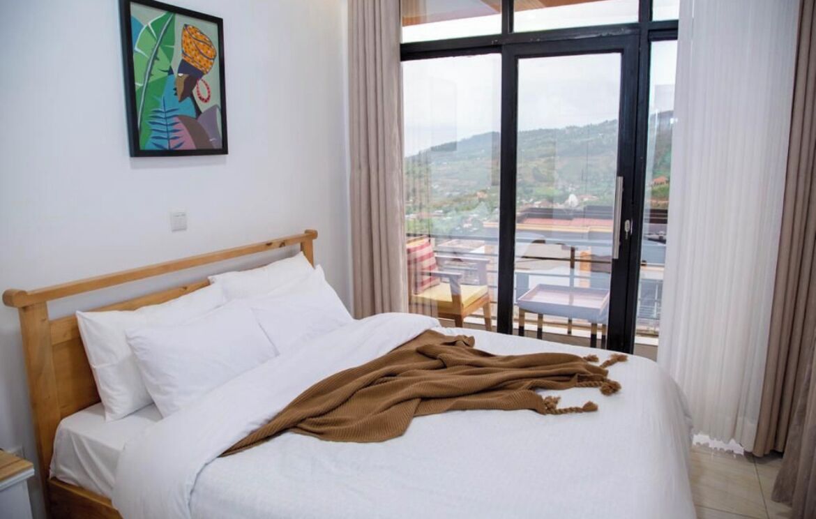 A hotel room with a large bed, a view of the city through the window, and a painting on the wall.