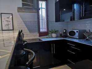 A modern kitchen with black cabinets, a stainless steel countertop, a microwave, and a coffee maker.