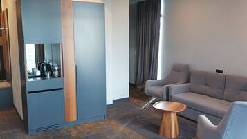 A modern hotel room with a grey sofa, a wooden side table, and a built-in coffee machine.