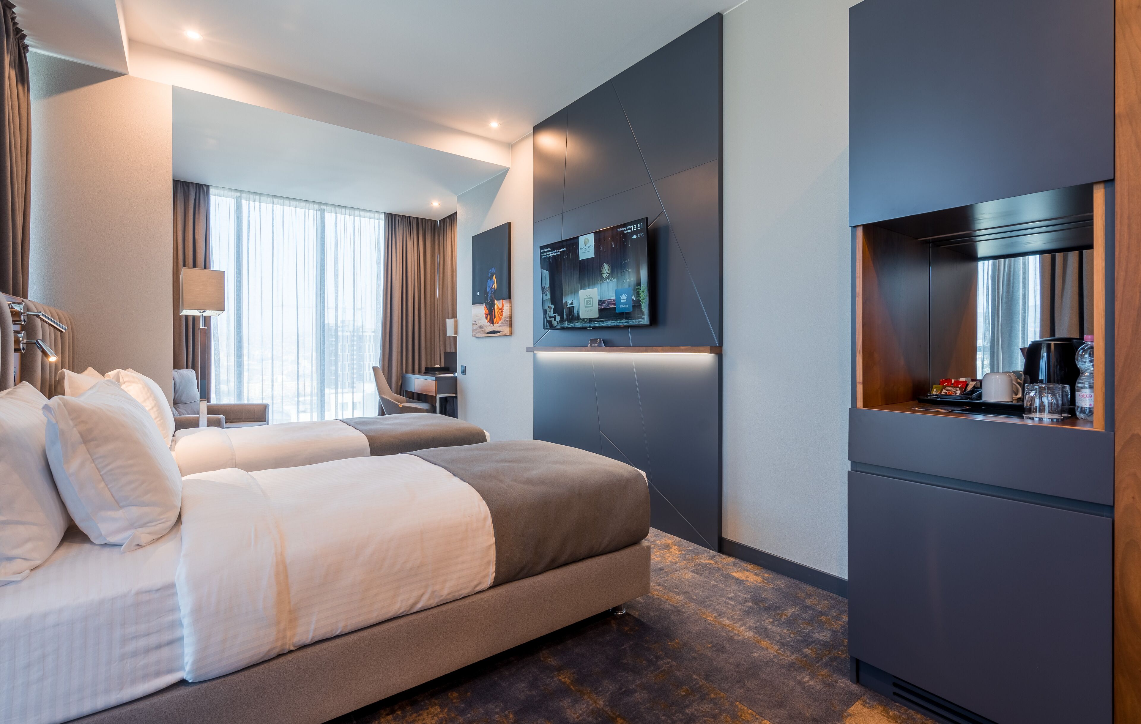 A modern hotel room with a large bed, a desk, a TV mounted on the wall, and a coffee machine.