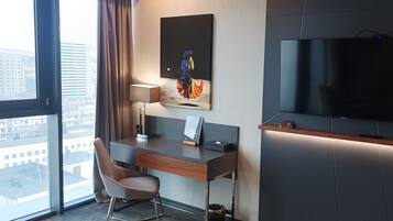 Habitación de hotel moderna con un gran ventanal, un escritorio con silla, un televisor de pantalla plana y un cuadro en la pared.