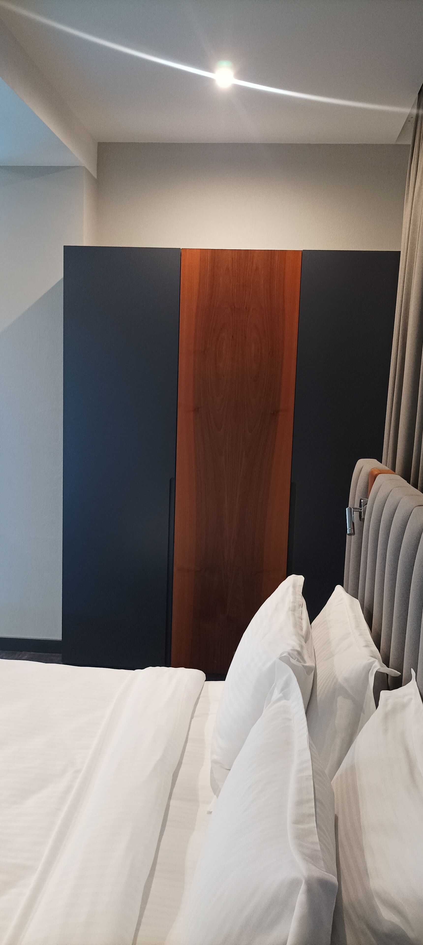 A modern hotel room with a bed, a wooden accent wall, and a grey headboard.