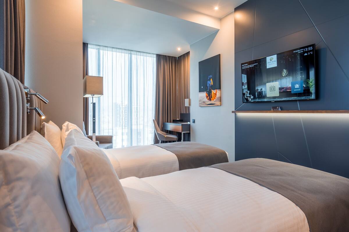 Hotellihuone, jossa on kaksi sänkyä, työpöytä, televisio ja ikkuna, jossa on verhot.
