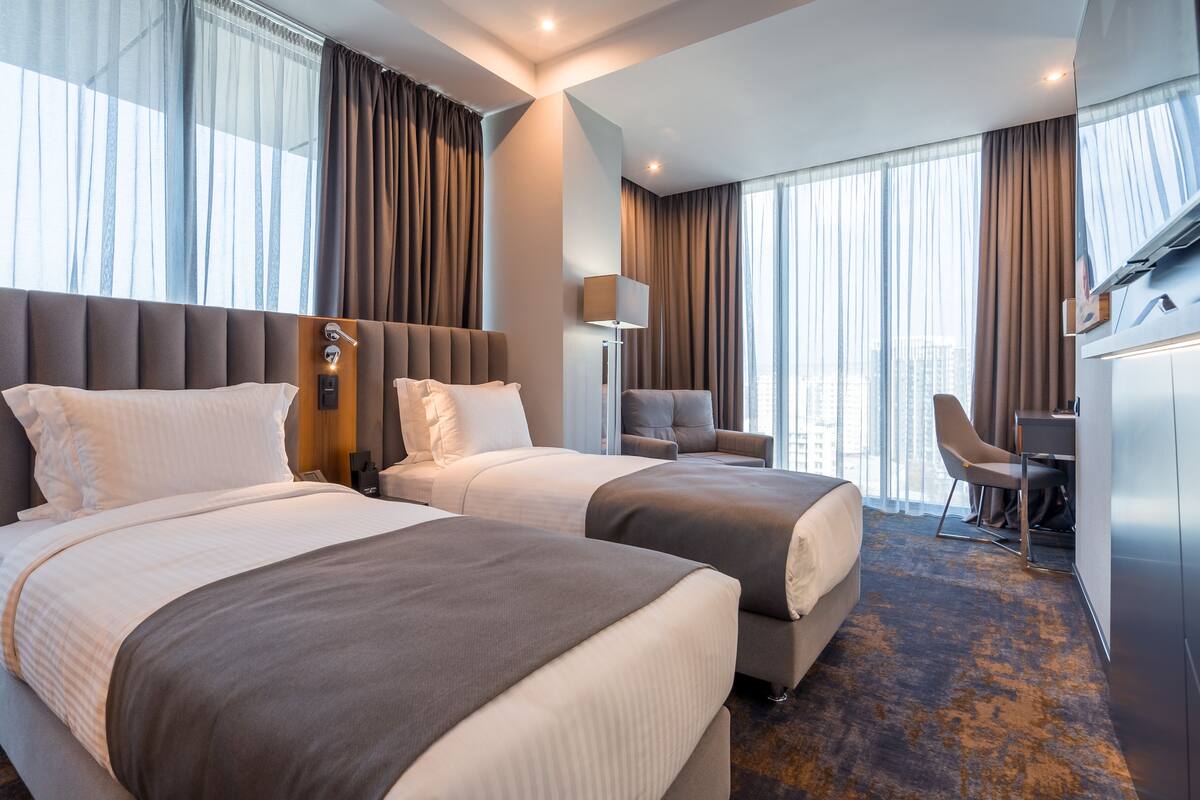 Hotellihuone, jossa on kaksi sänkyä, työpöytä ja tuoli.