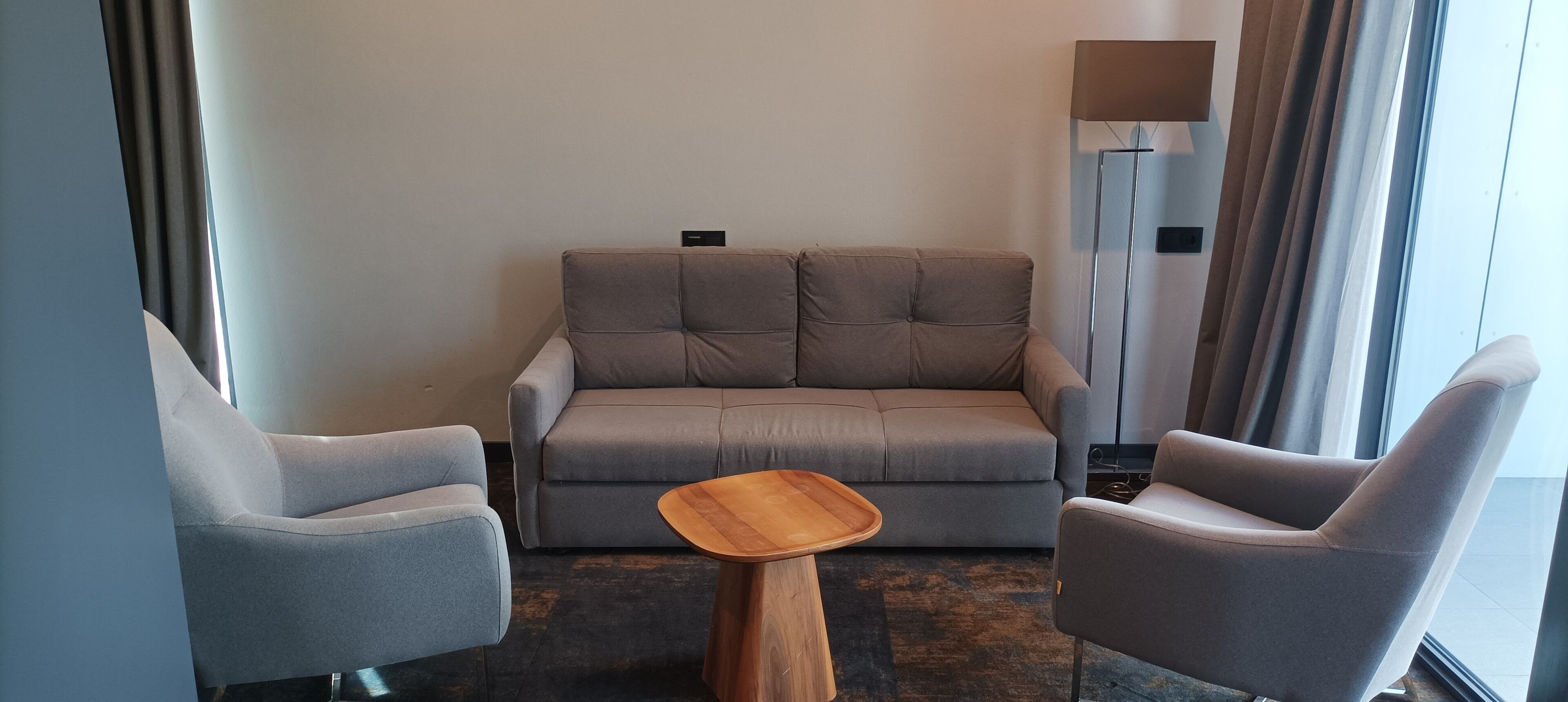 A modern living room with a grey sofa, two grey armchairs, and a wooden coffee table.