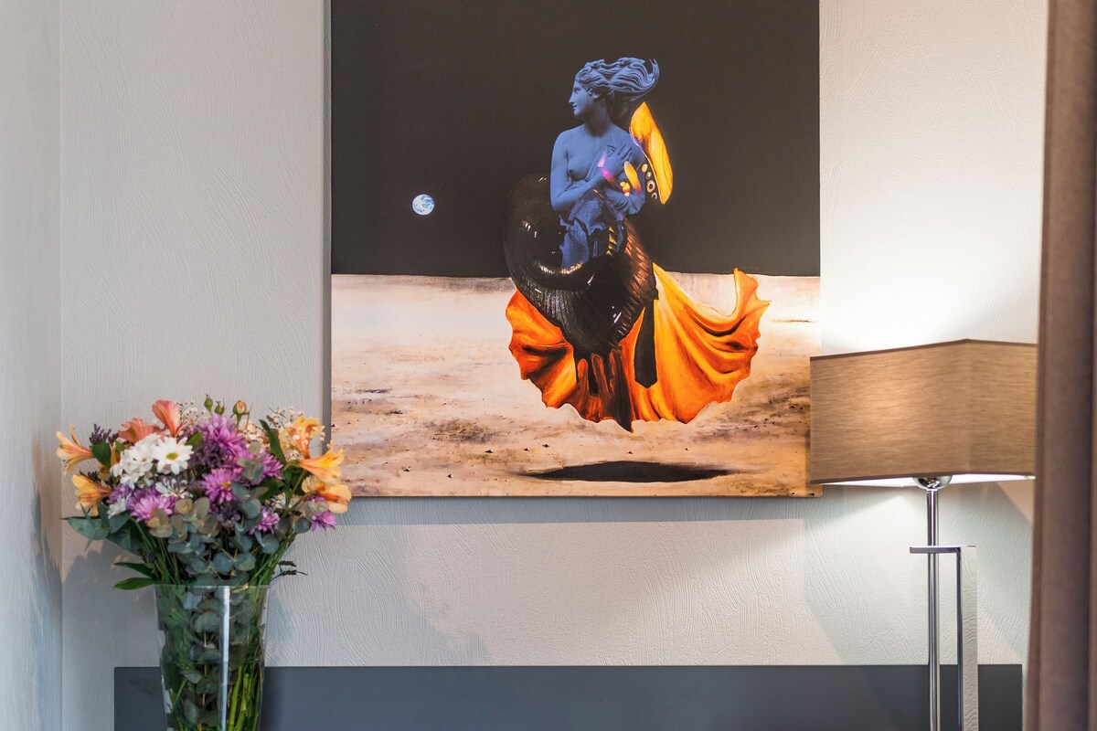 A modern desk with a vase of flowers, a lamp, and a painting on the wall.