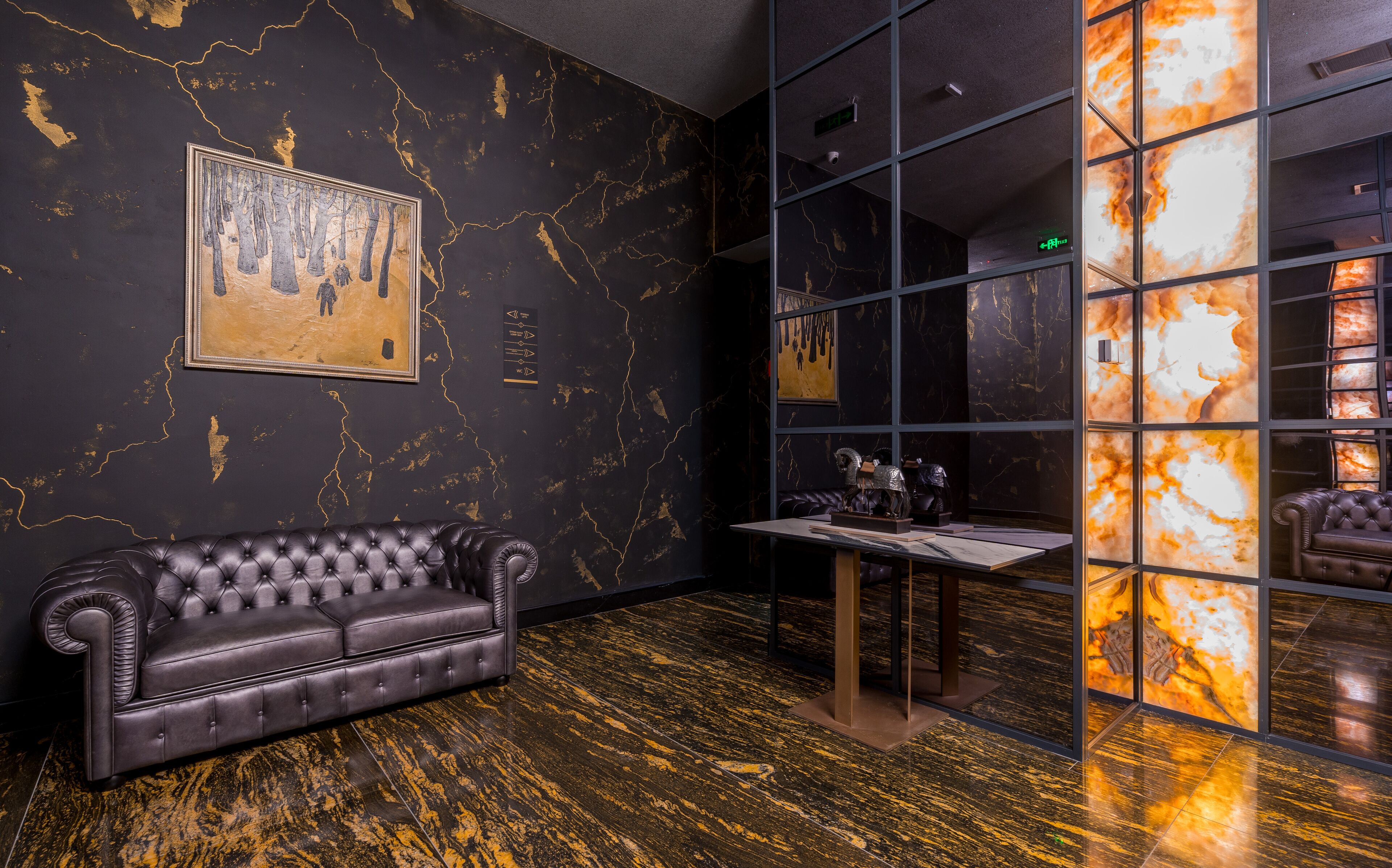 A room with a dark, marble-patterned wall, a tufted leather sofa, and a glass partition with a reflective surface.