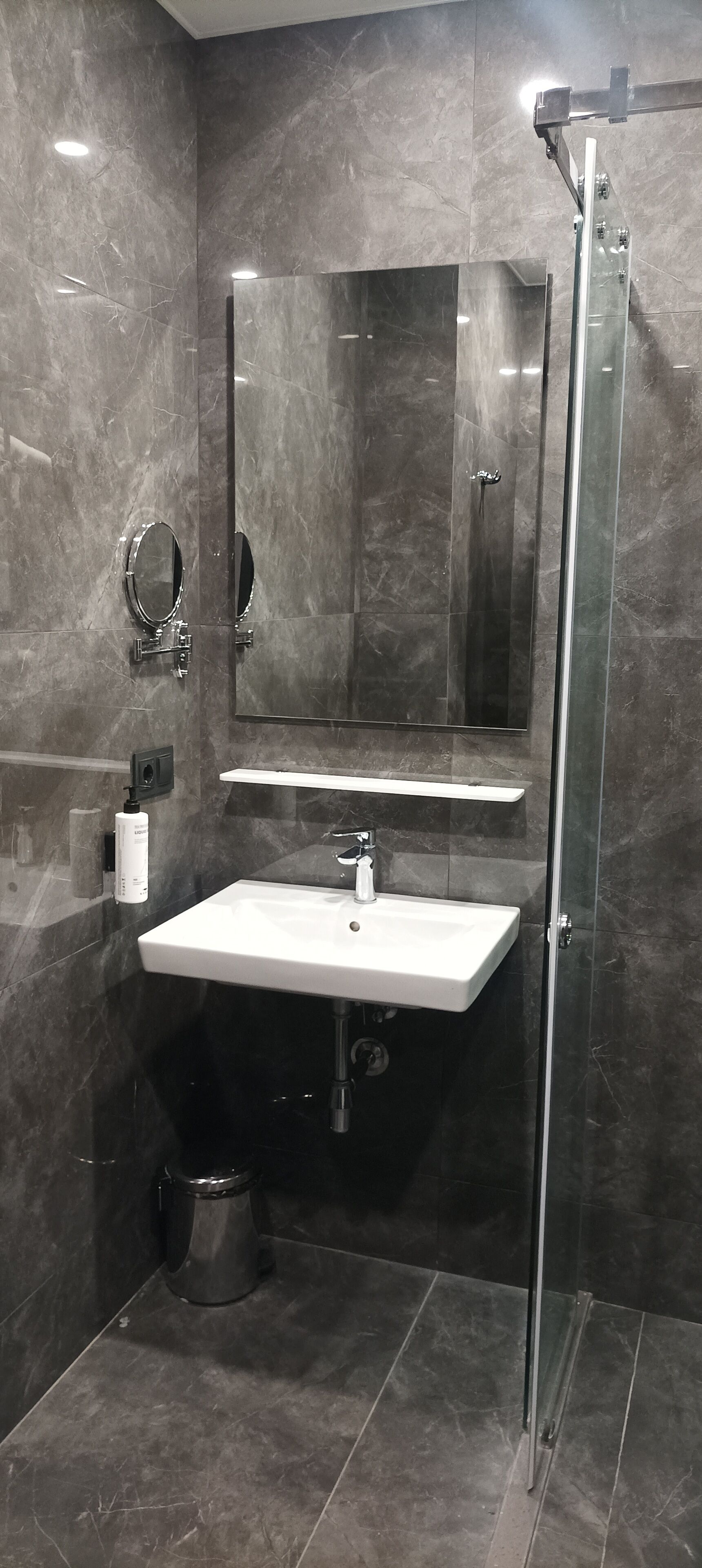 A modern bathroom with a glass shower enclosure, a white sink, and a large mirror.