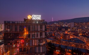 A modern hotel with a prominent sign, surrounded by a densely built urban area at dusk. -  Onyx City Center (Tbilisi)