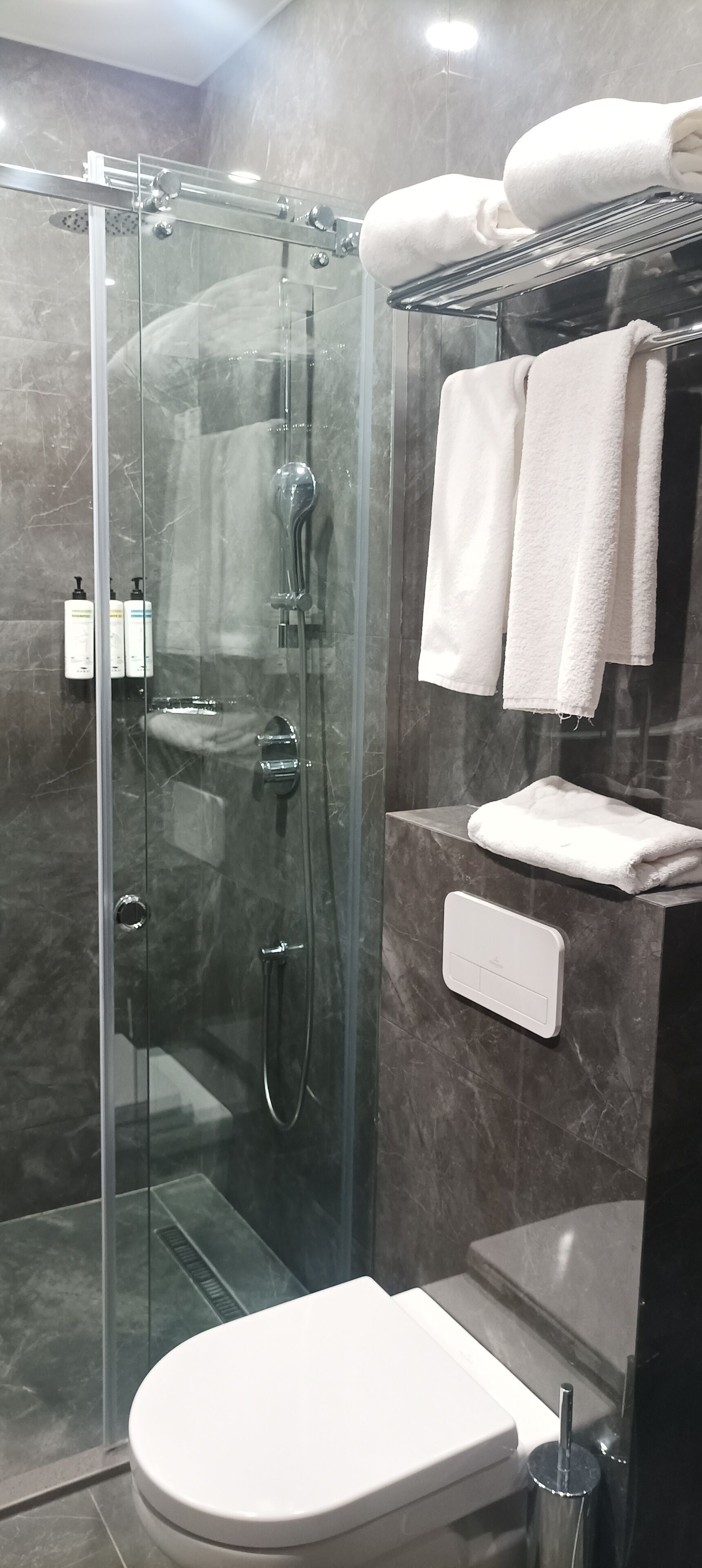 Une salle de bain moderne avec une douche à parois de verre, des toilettes et un porte-serviettes avec des serviettes pliées.