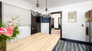 A modern kitchen with a wooden countertop, pendant lights, and a view into the dining area. - Casa Del Exotique | Walk Everywhere | AC | Beach (Traverse City)