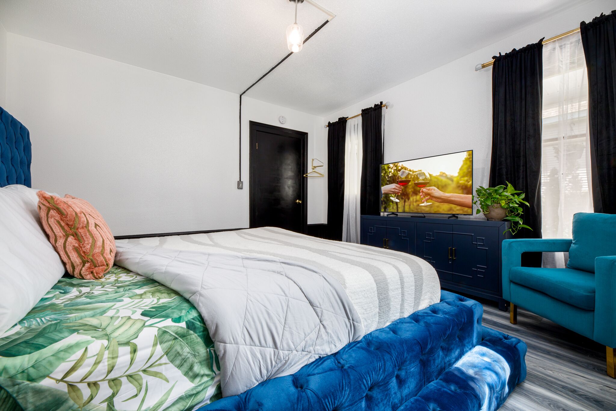 A modern bedroom with a bed, a blue sofa, a TV, and a plant.