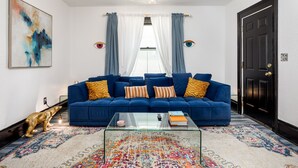 A living room with a blue sofa, a glass coffee table, and a colorful rug. - Casa Del Exotique | Walk Everywhere | AC | Beach (Traverse City)