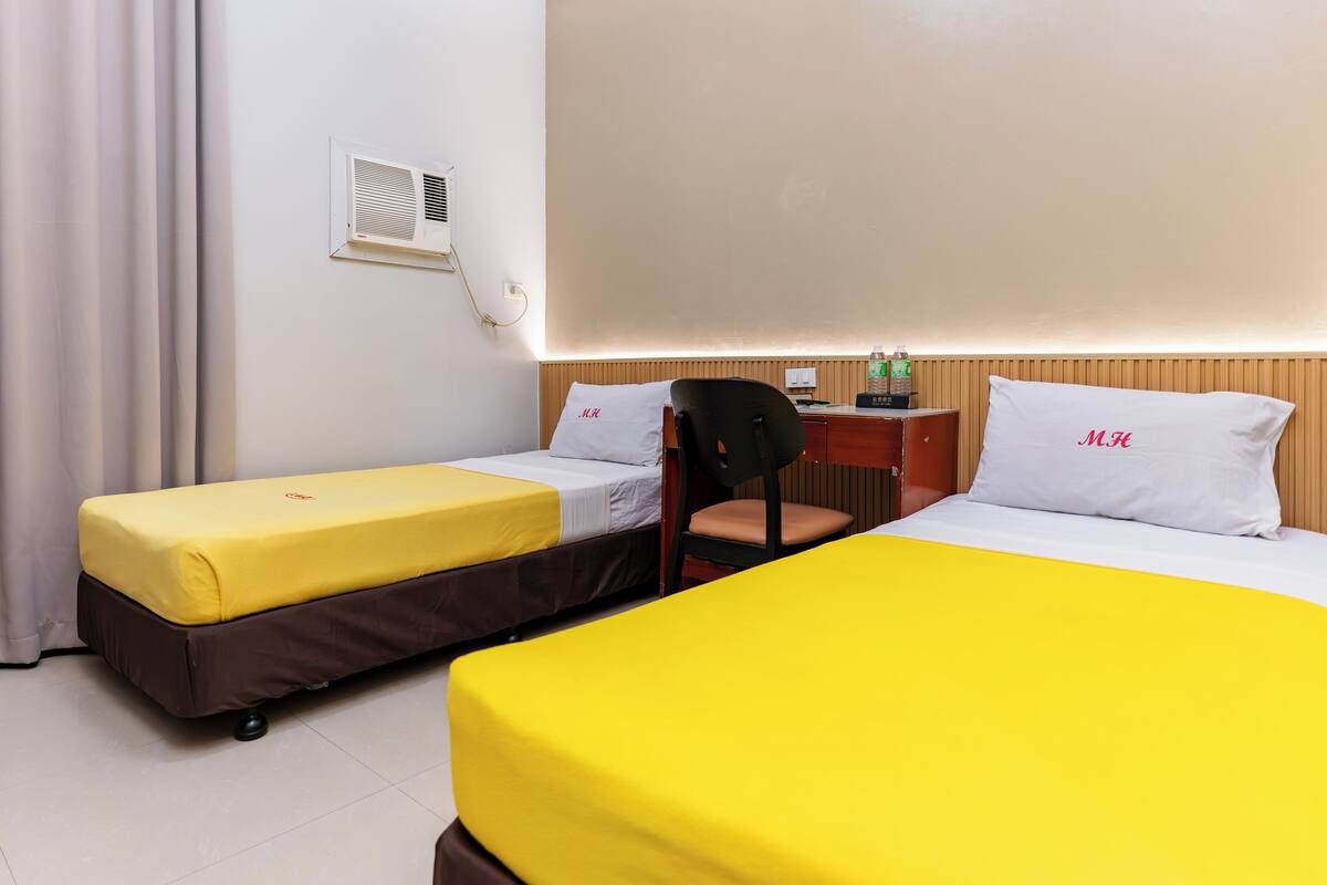 A hotel room with two beds, a chair, a desk, and a wall-mounted air conditioner.