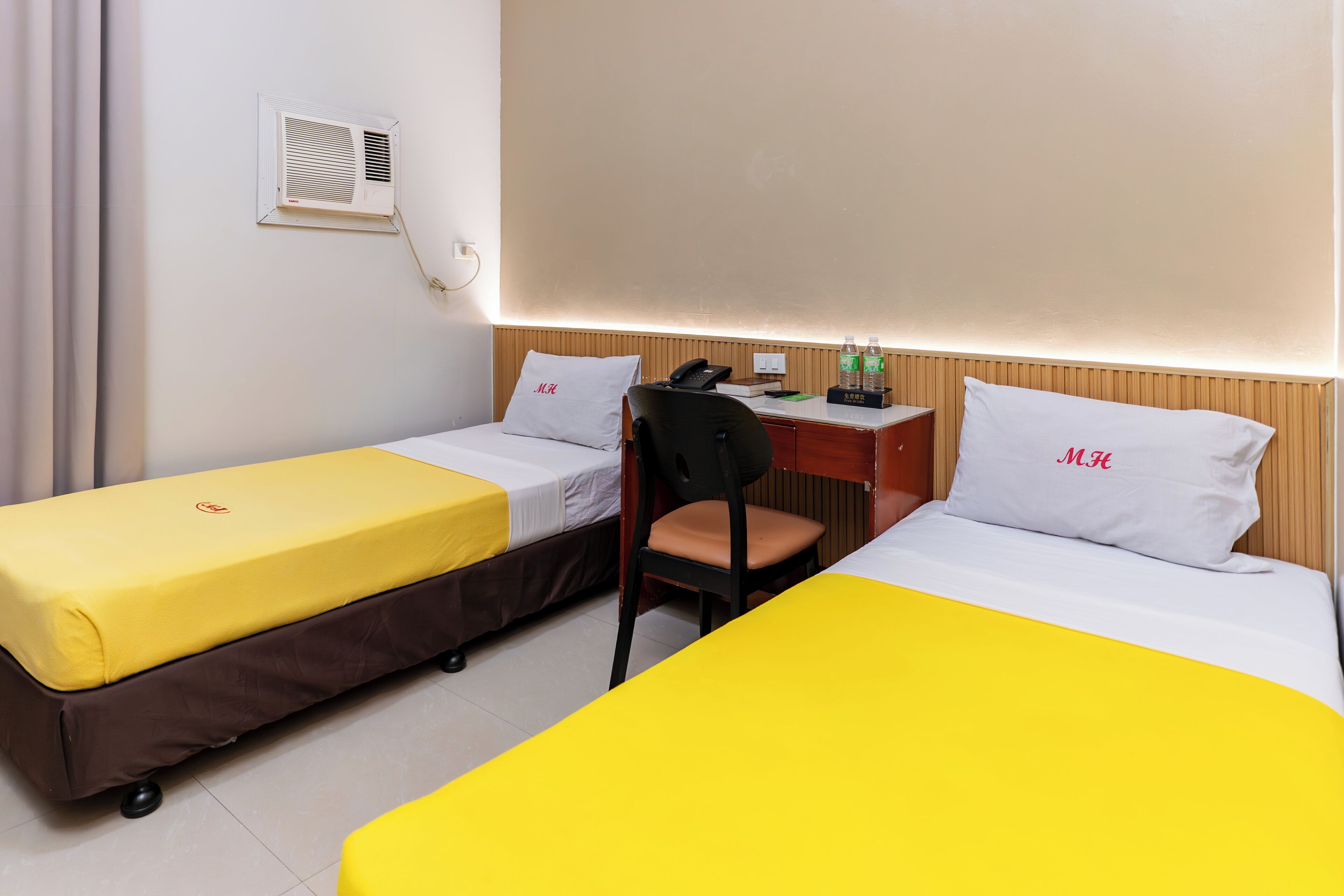 Habitación de hotel con dos camas, un escritorio, una silla, un teléfono y aire acondicionado instalado en la pared.