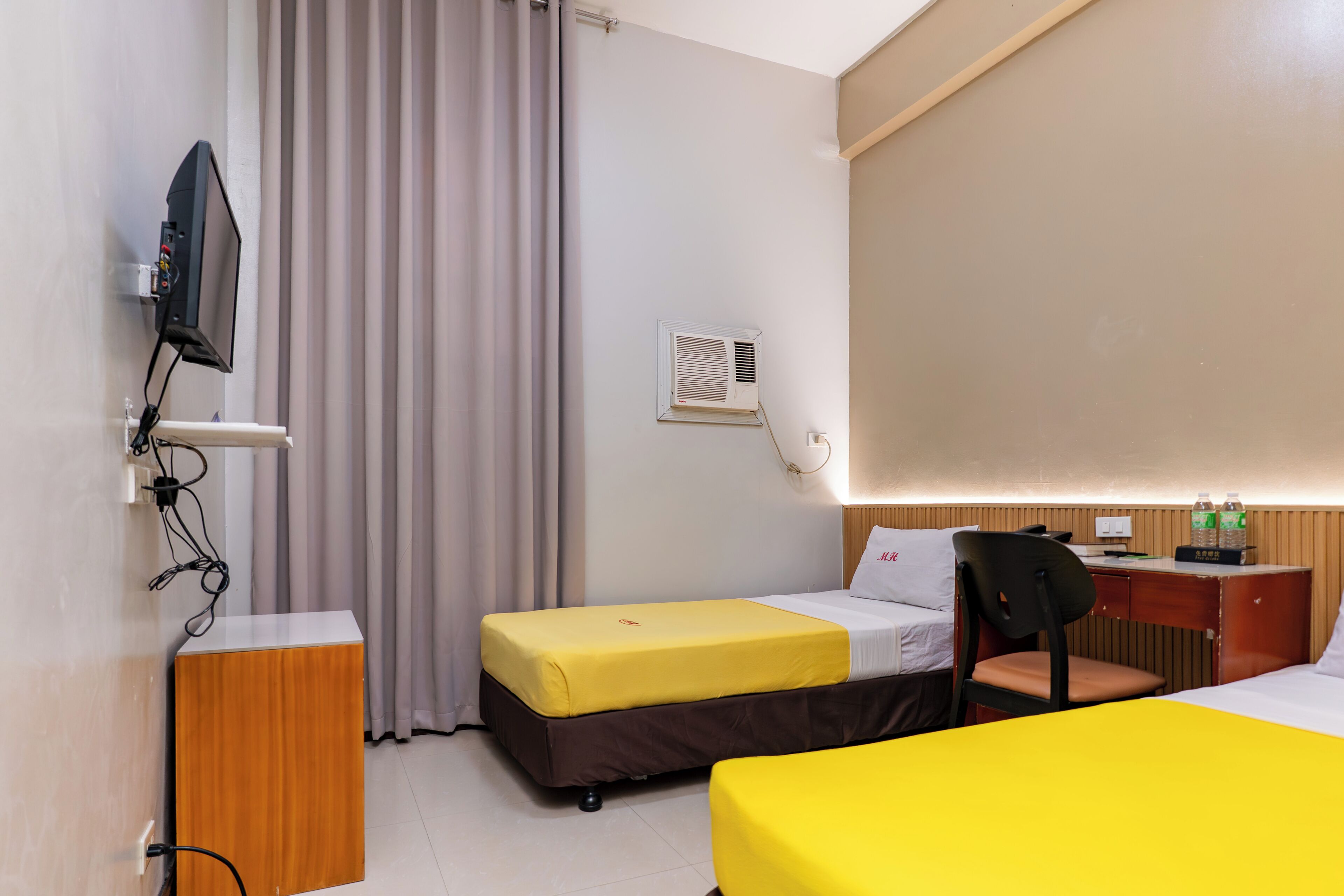 A hotel room with a bed, a desk, a chair, a television, and an air conditioning unit.