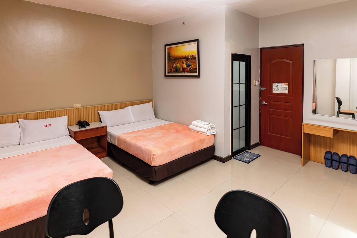 A hotel room with two beds, a desk, a chair, a mirror, a door, and a painting on the wall.