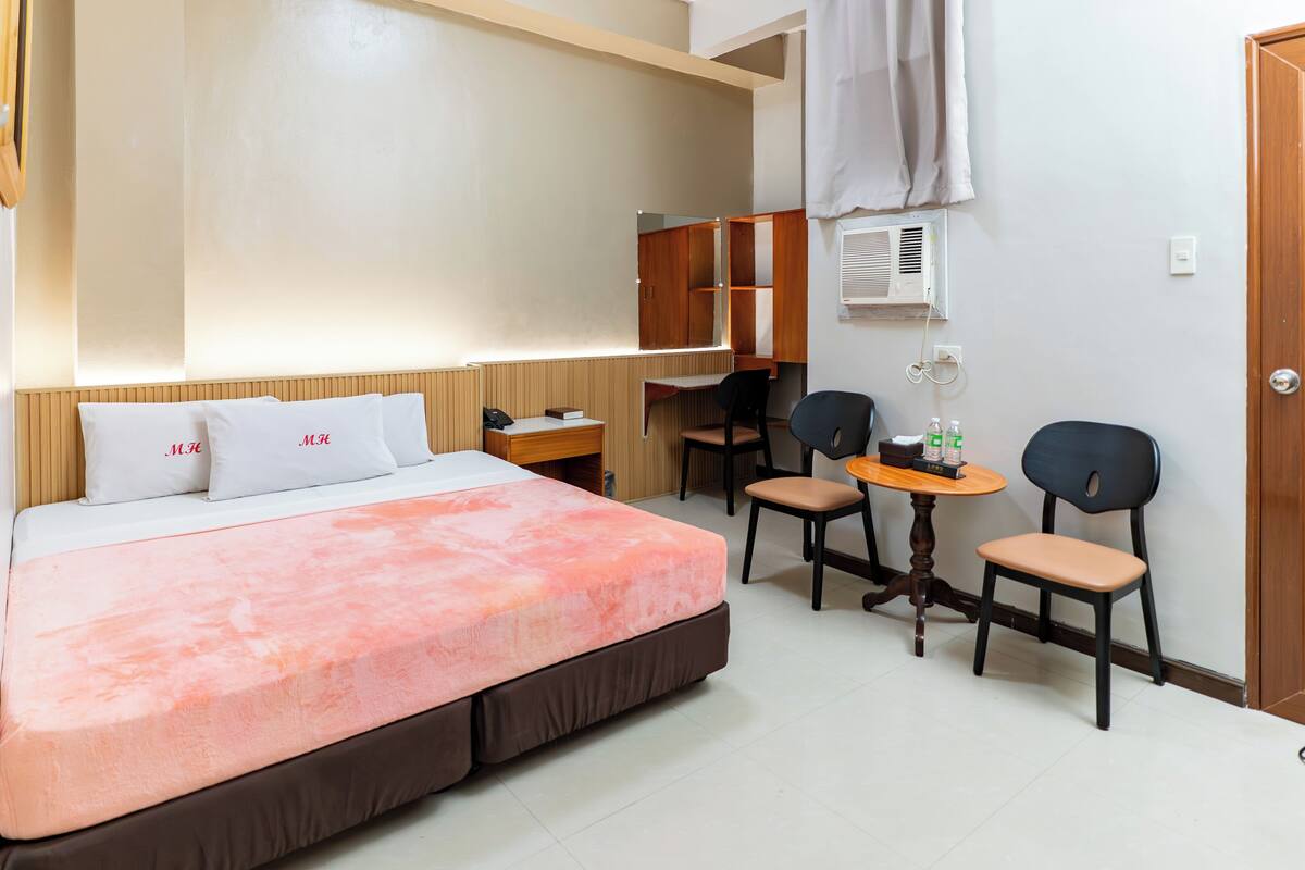 A hotel room with a bed, desk, two chairs, a small table, and a wardrobe.