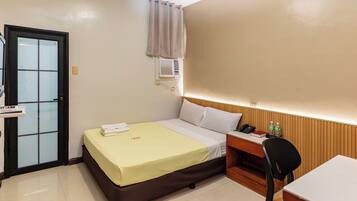 Una habitación de hotel con cama, escritorio, silla, puerta y unidad de aire acondicionado.