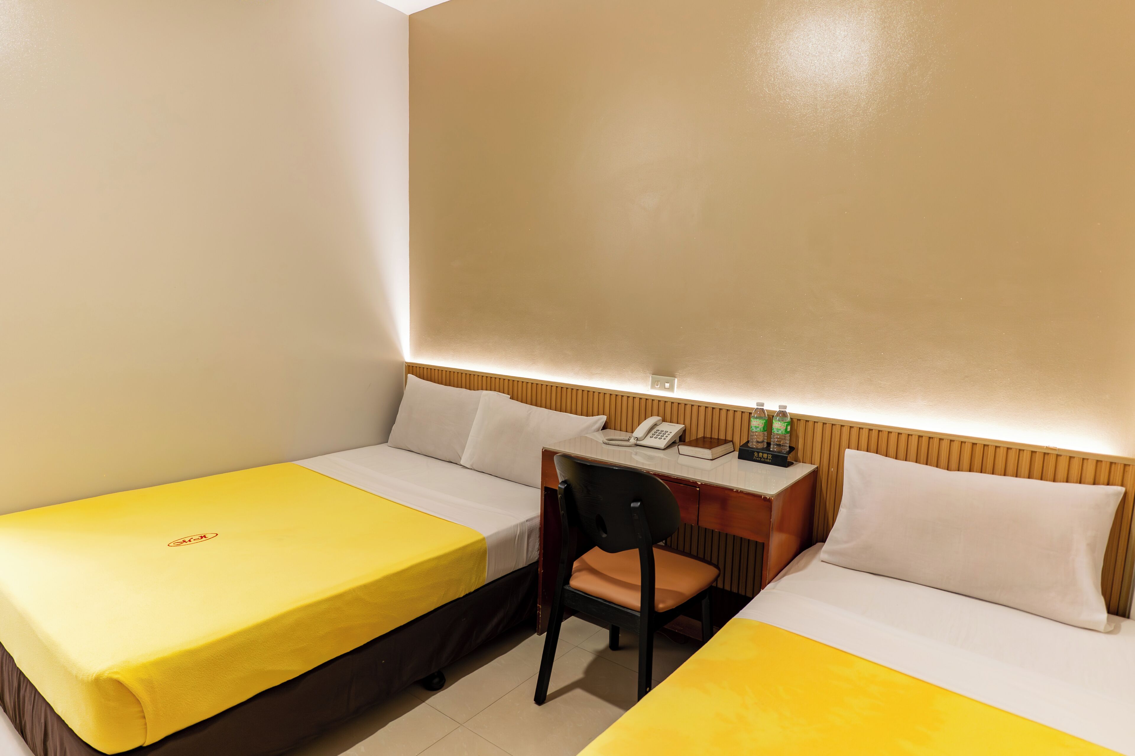 A hotel room with two beds, a desk, a chair, a telephone, and a bottle of water.