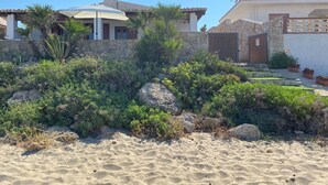 En fastighet vid kusten med en sandstrand, en stenmur och ett hus med ett tak täckt av tegelpannor.