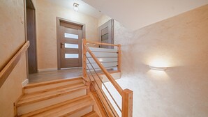 A wooden staircase with a handrail, a door with frosted glass panels, and a wall-mounted light fixture. - Apartamenty Sun & Snow Kaniówka (Bukowina Tatrzanska)