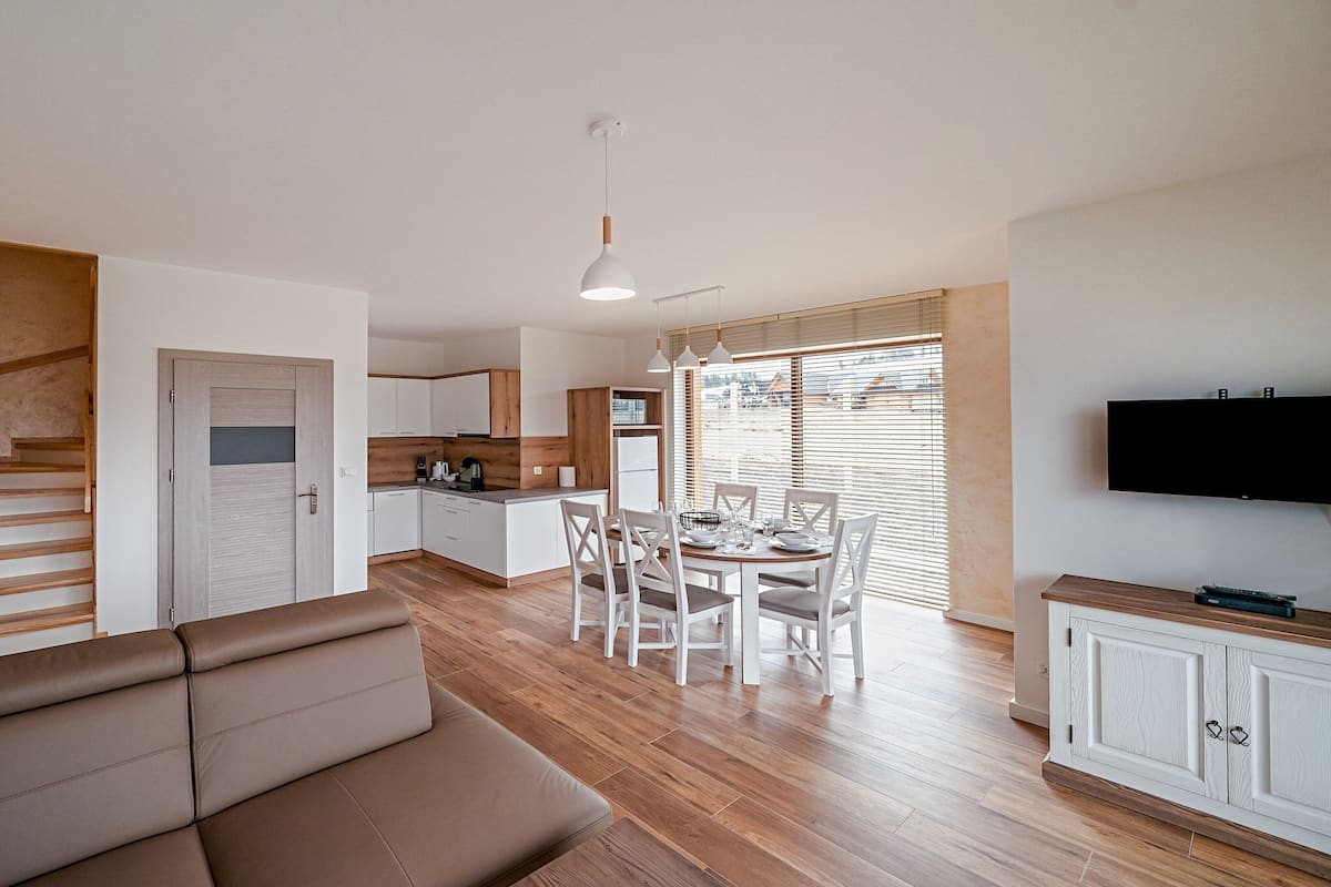 A modern living space with a wooden staircase, a dining area, and a kitchen.
