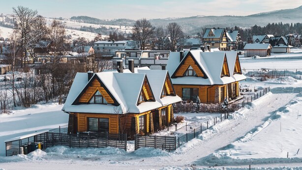 A row of wooden cabins with snow-covered roofs, set in a snowy landscape with a view of a village in the background. - Apartamenty Sun & Snow Kaniówka (Bukowina Tatrzanska)