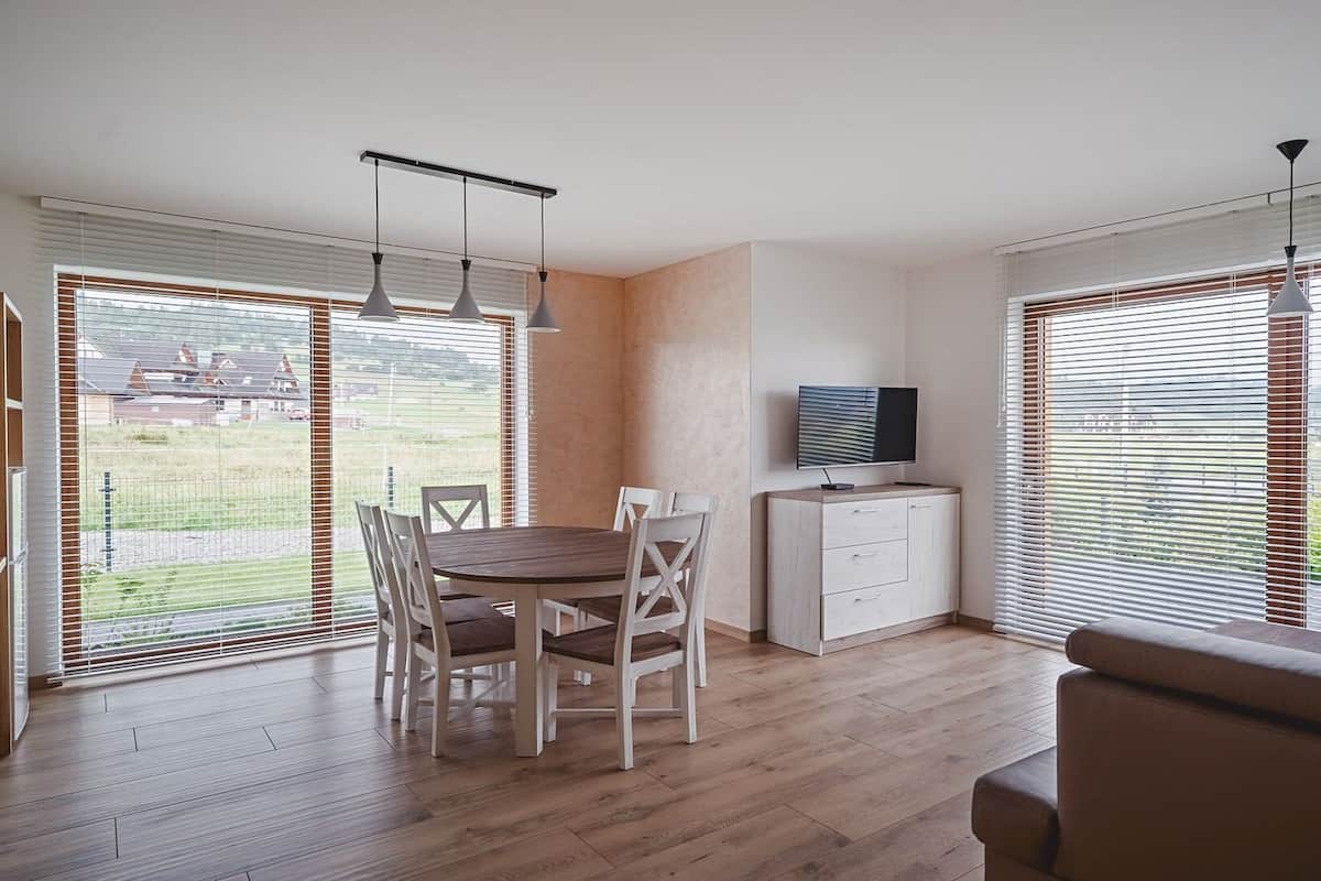 A modern kitchen with a dining area, large windows, and a flat-screen TV.