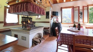 Una cocina rústica con estufa de leña, un ventanal con vistas a un paisaje montañoso y una zona de comedor con una mesa dispuesta para dos.