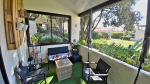 Un patio cubierto con un sofá, dos sillas, una mesita y plantas en macetas.
