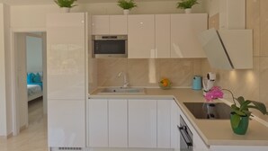 A modern kitchen with white cabinets, a built-in microwave, a sink, and a small countertop area. There are two potted plants on the cabinets and a vase with flowers on the countertop.
